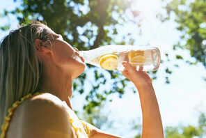 Frau trinkt aus einer Wasserflasche mit einer Zitrone drin © Adobe Stock Iuricazac